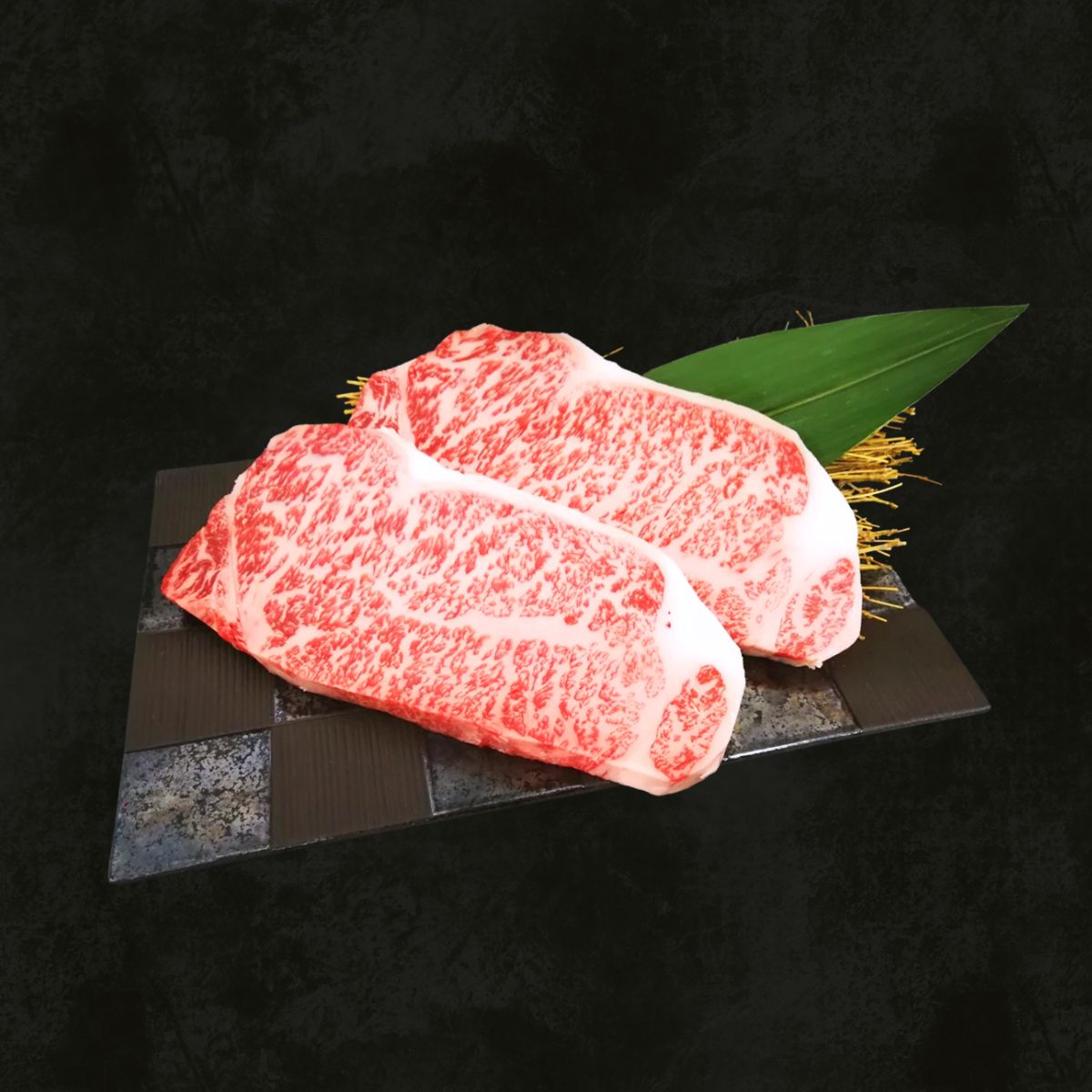 Marbled wagyu beef striploin steaks on a serving tray with green leaf