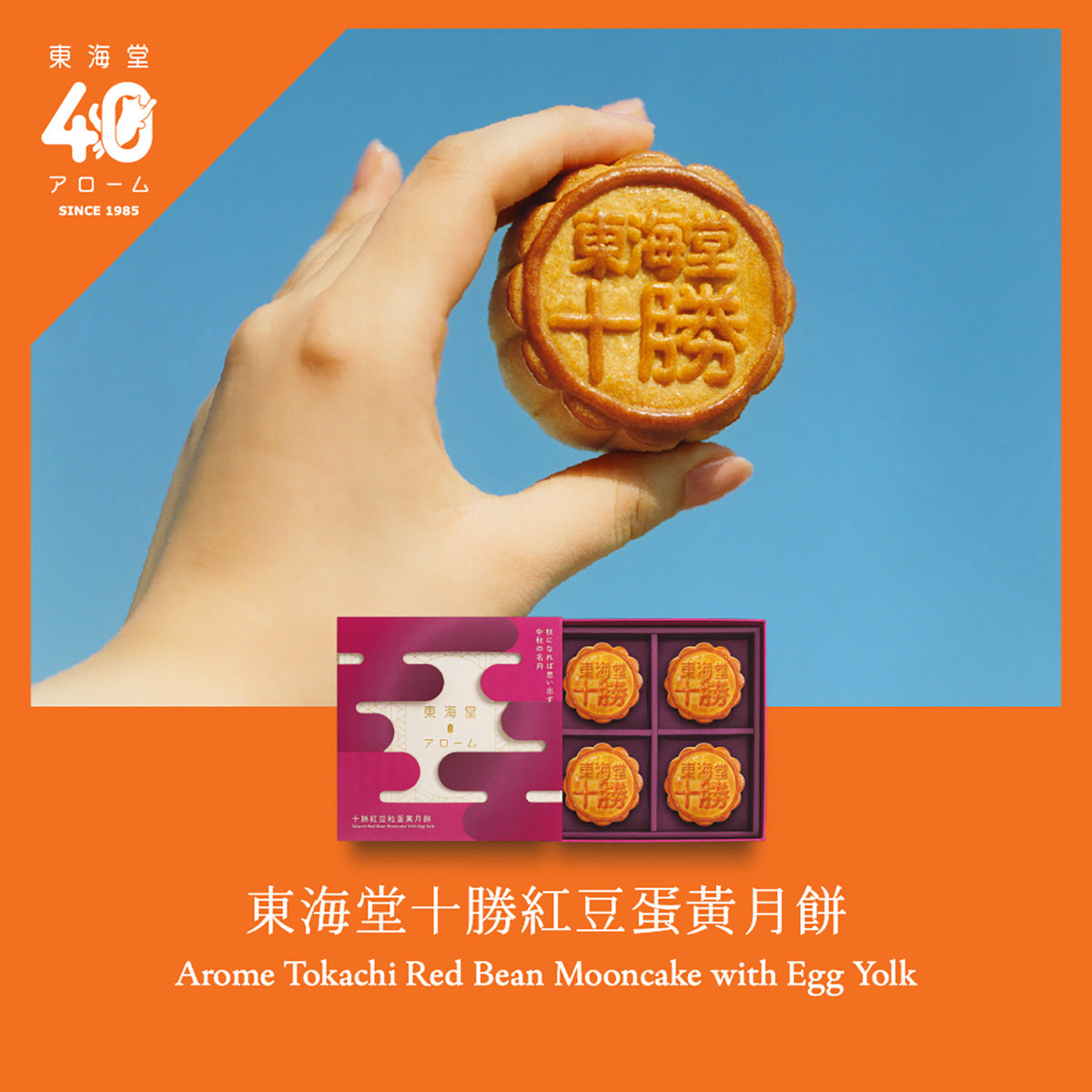 Red bean mooncake with stamped top, held in a hand beside a boxed set