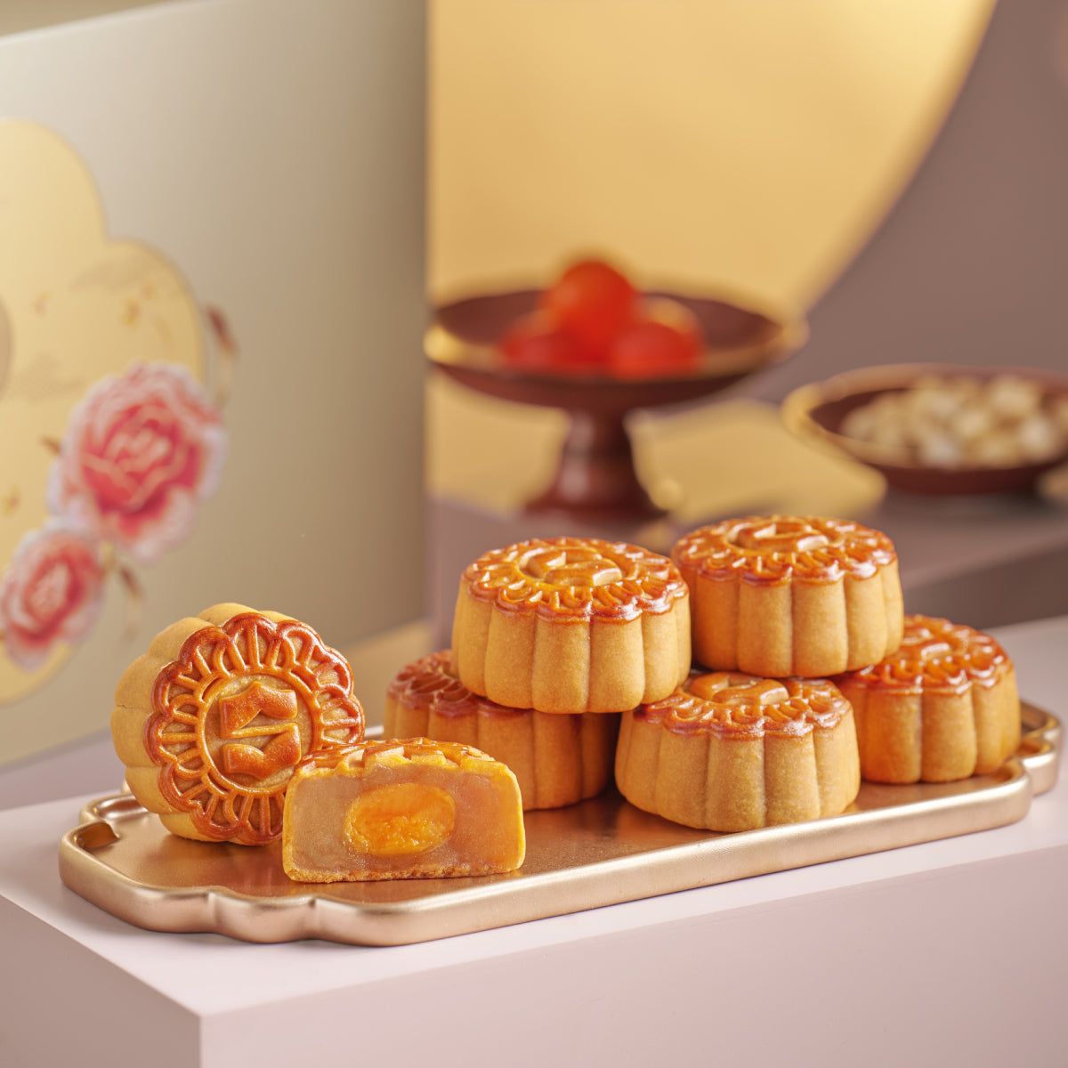 Mini mooncakes with glossy orange patterned tops and visible egg-yolk filling on a tray