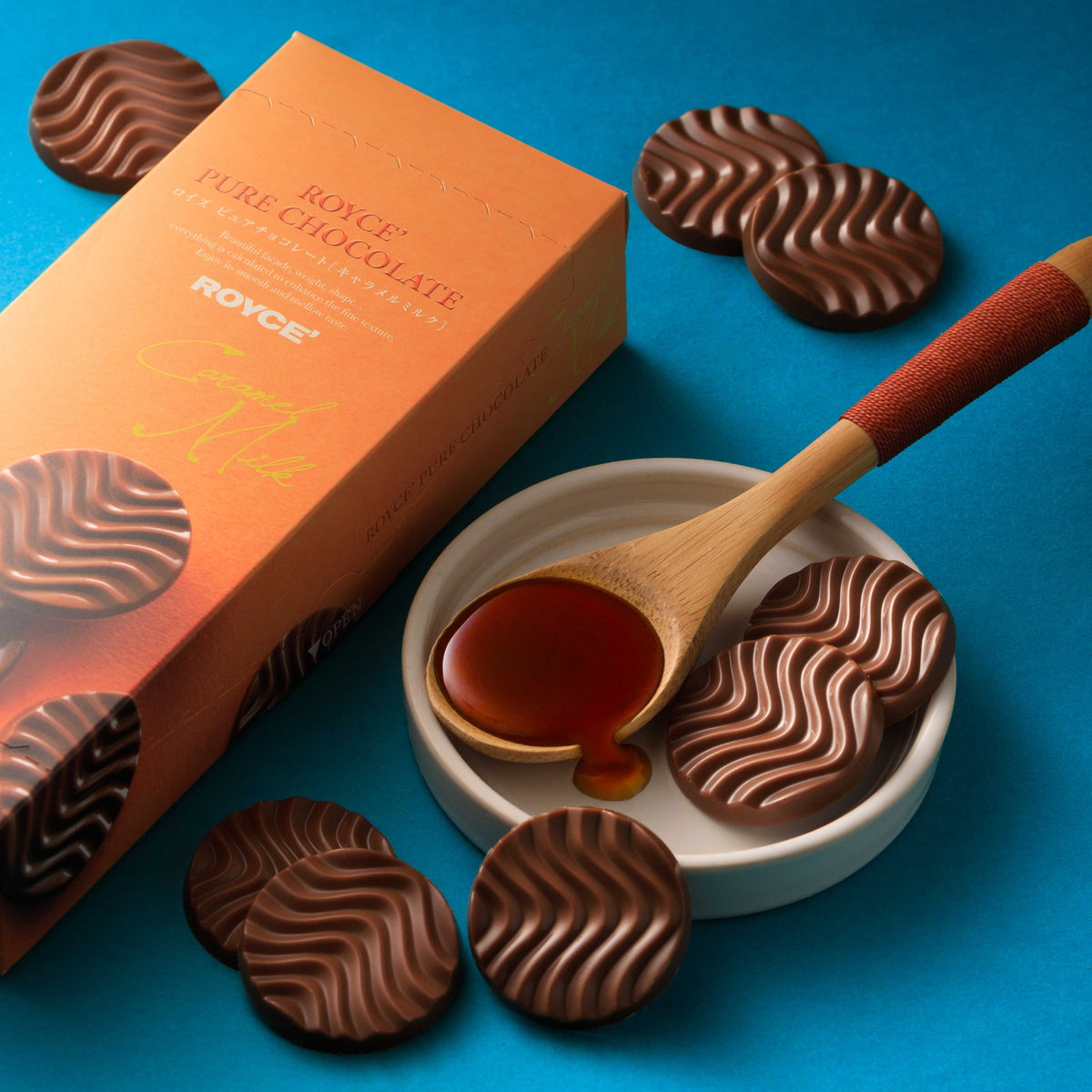 Caramel milk chocolates in heart shapes beside open box and wooden spoon.