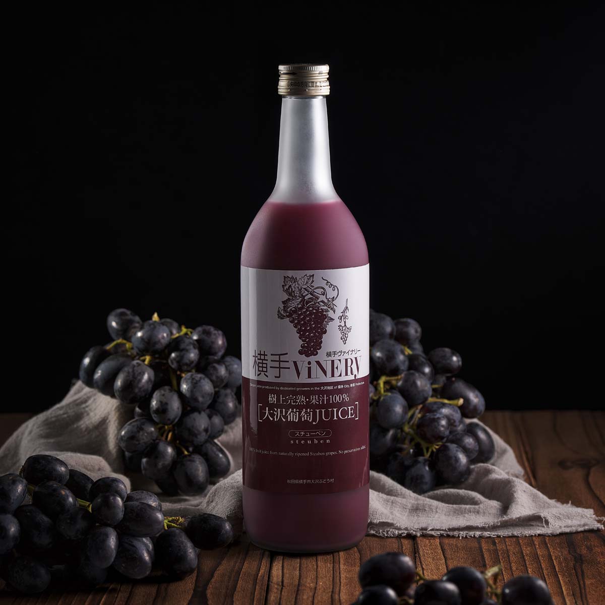 Bottled grape juice with gold cap, dark purple label, surrounded by grapes