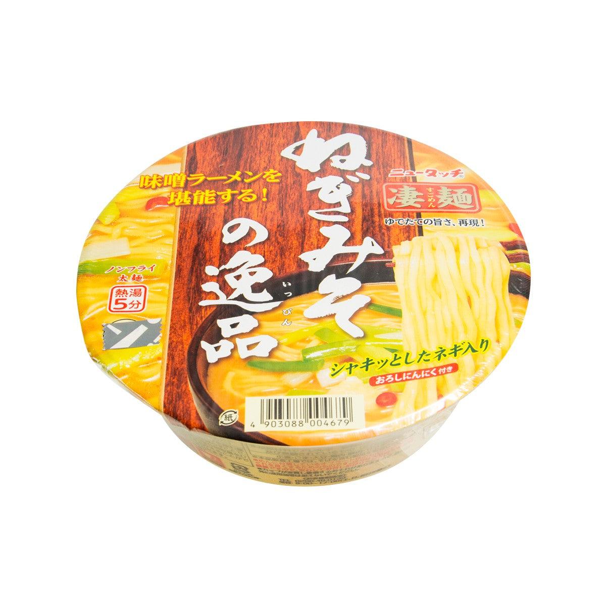 Instant ramen cup, yellow broth with chunky noodles and leek pieces visible