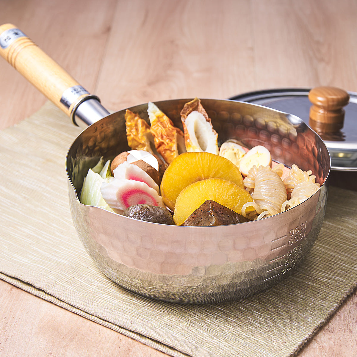 Hammered stainless steel sauce pot with wooden handle, filled with ingredients