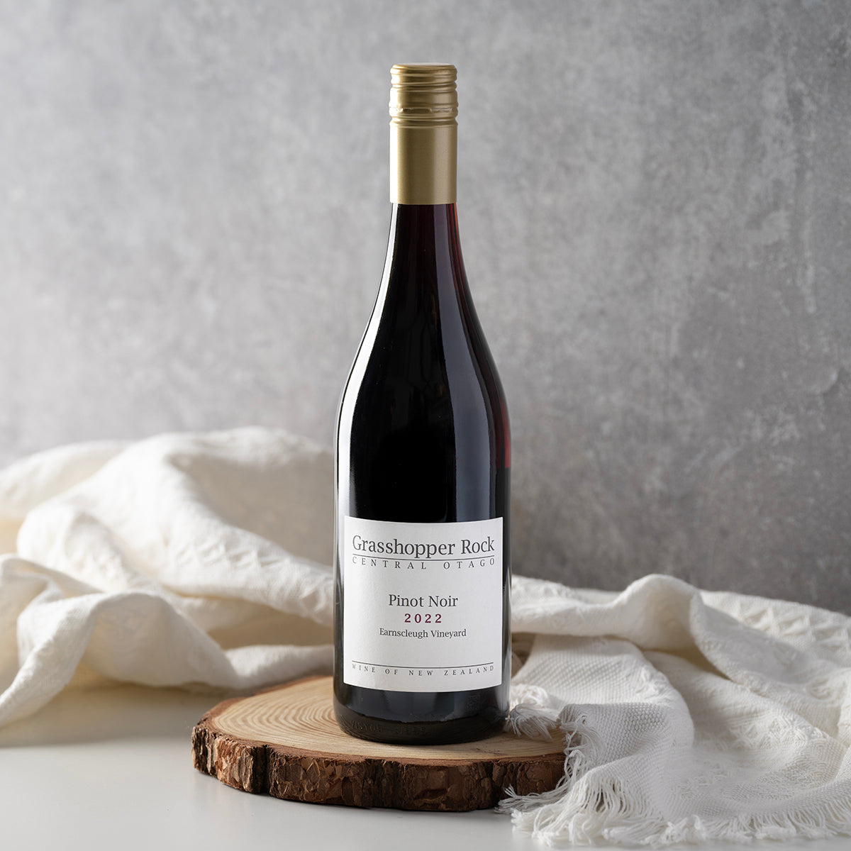 Pinot Noir wine bottle on wooden slice with draped cloth, gold foil neck