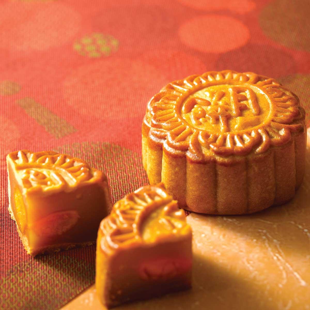 Golden-brown traditional mooncake with embossed pattern, with two cut slices.