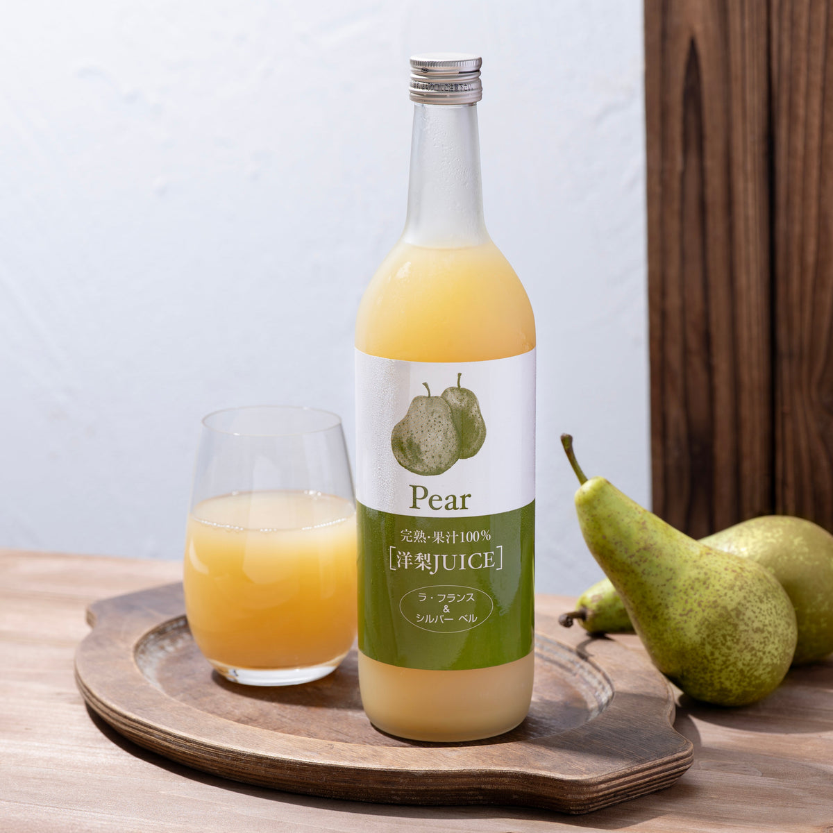 Pear juice bottle with glass of juice and pears on wooden tray