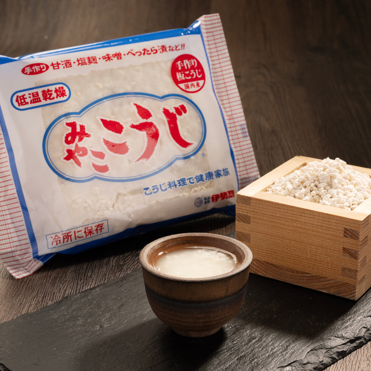 Malted rice packet with wooden bowl and scoop of pale grains, angled view