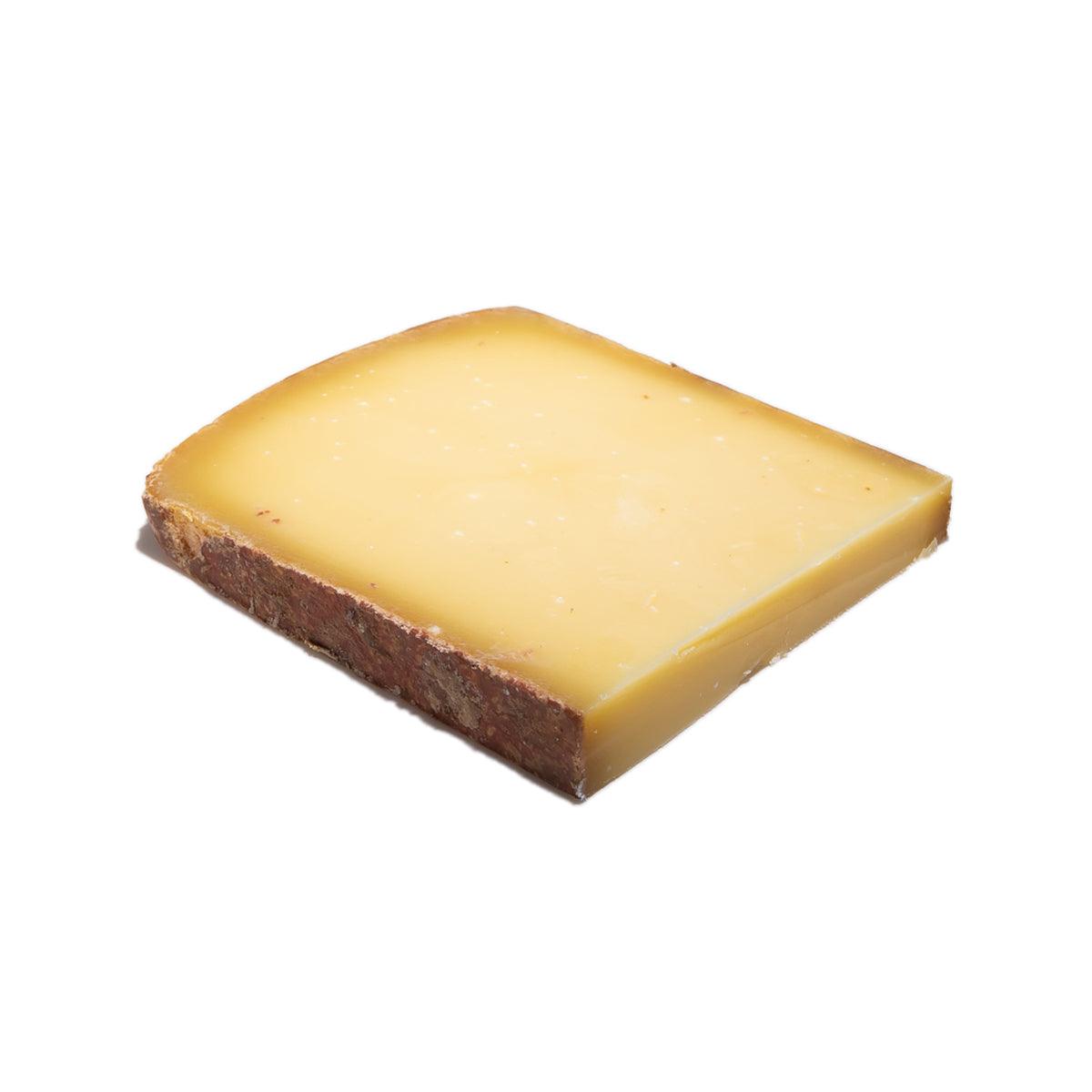 Raw milk Comte-style cheese wedge, pale yellow interior with dark rind edge