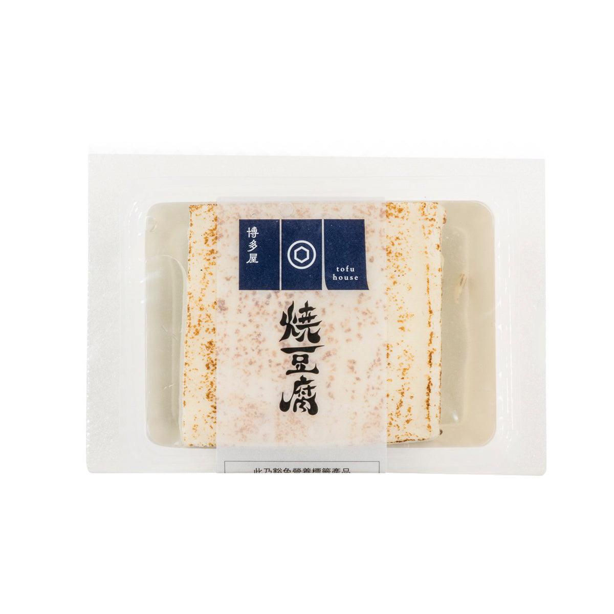 Grilled tofu block in sealed tray, off-white with orange spice speckles.