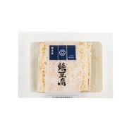Grilled tofu block in sealed tray, off-white with orange spice speckles.