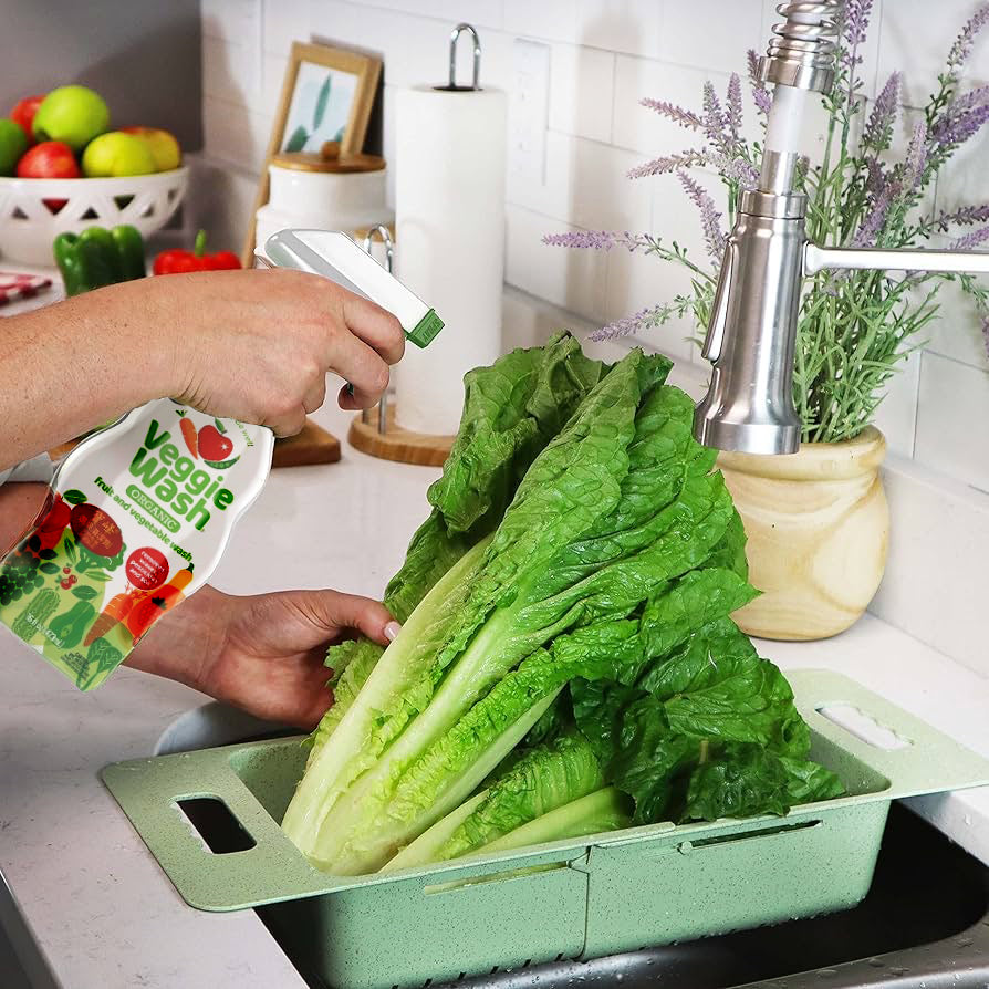Hand holding spray bottle rinsing leafy greens in sink.