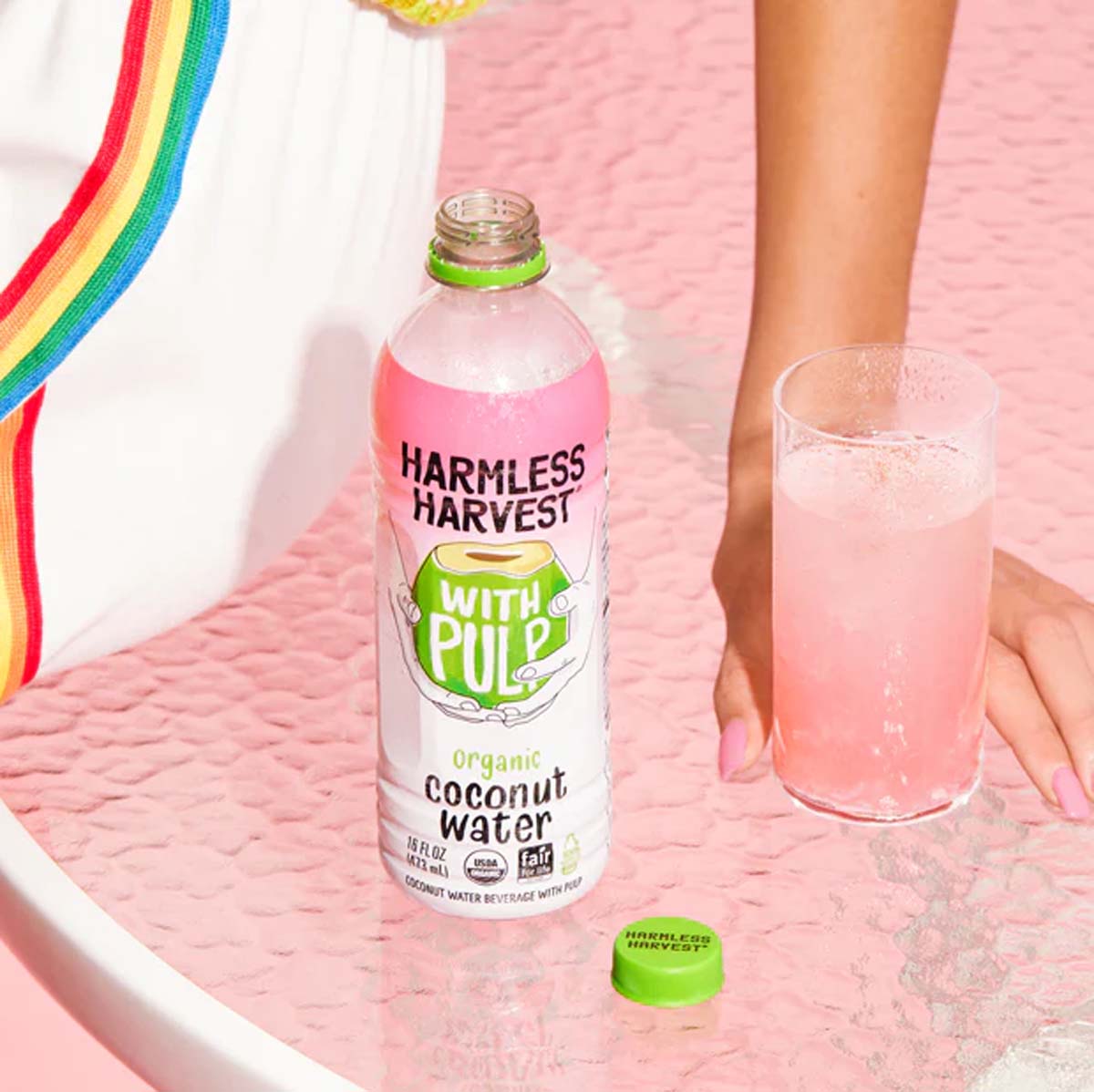 HARMLESS HARVEST coconut water bottle with pulp, green cap, with glass in hand