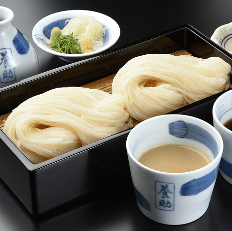 Dried udon noodles in white tray with bowls of broth and garnish