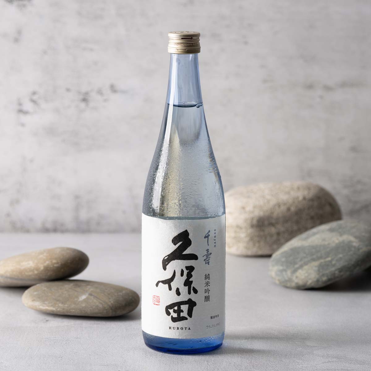KUBOTA Junmai Ginjo sake bottle with front label and gold cap on blue-tinted glass