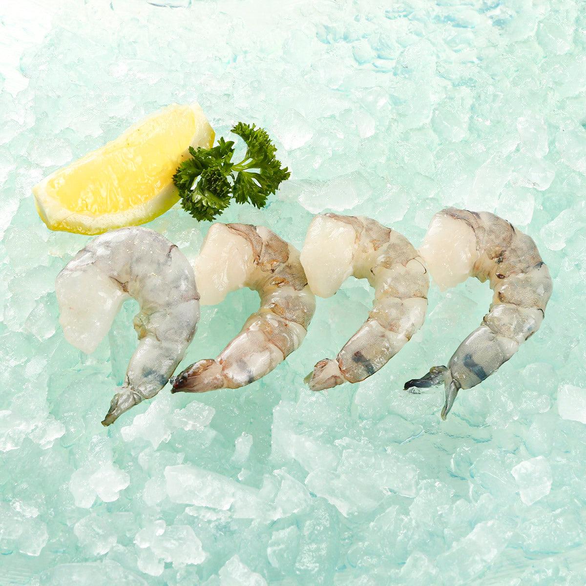 Raw peeled deveined tail-off shrimp on ice, with lemon wedge and parsley