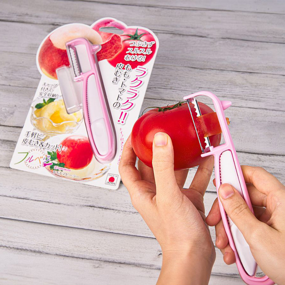 Handheld pink and silver peeler slicing a red tomato; countertop background