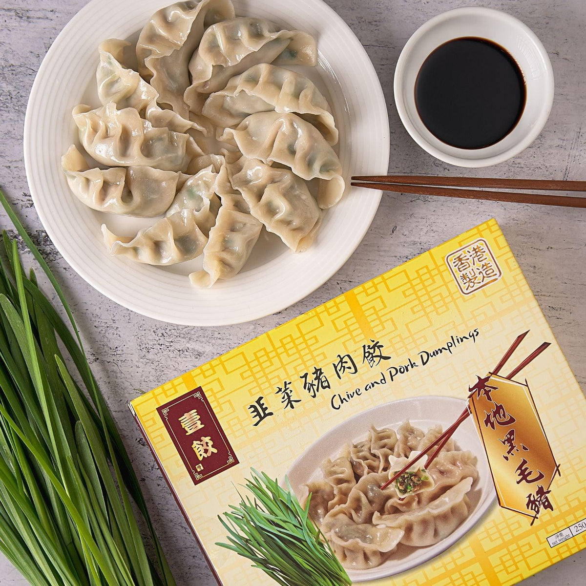 Chive and pork dumplings on plate with dipping sauce, plus boxed pack