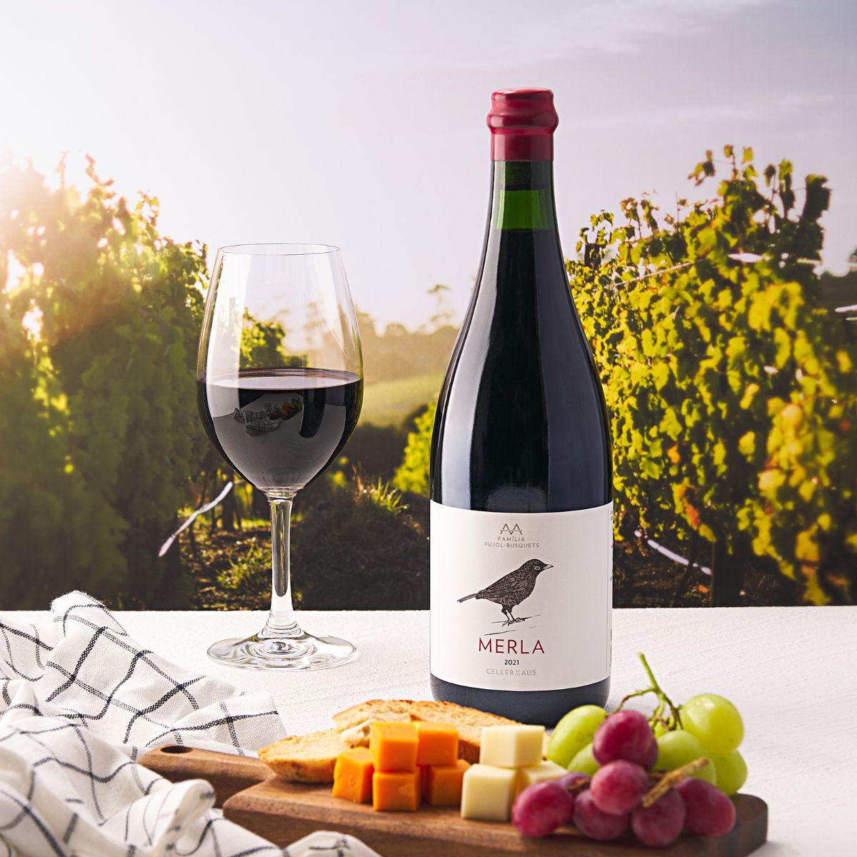 Merla wine bottle with red cap beside a wine glass and cheese on table