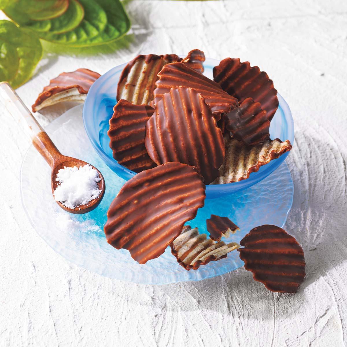 Chocolate potato chips with ridged coating on blue plate, sea salt flakes