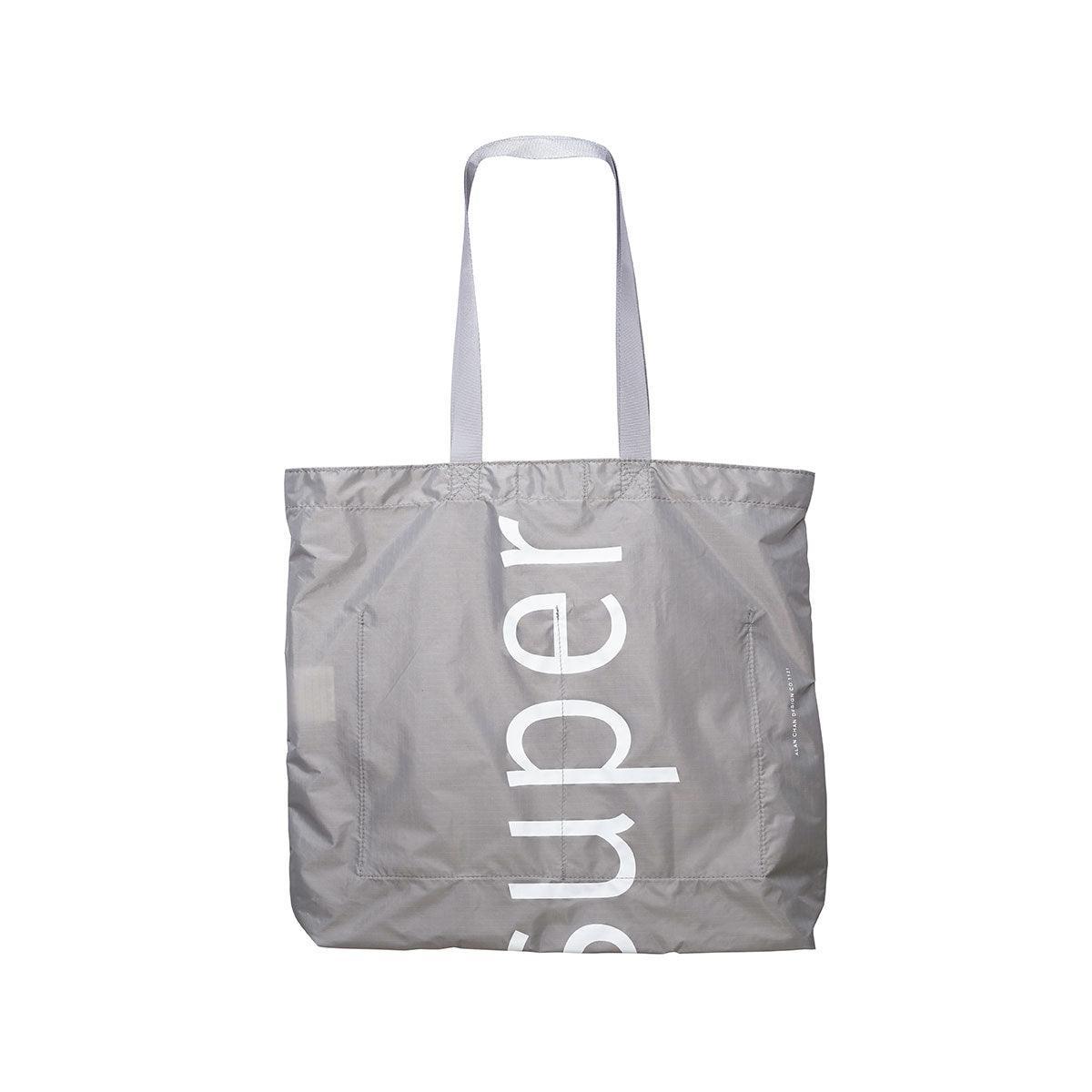 Taupe foldable tote bag with long handles and vertical white logo print