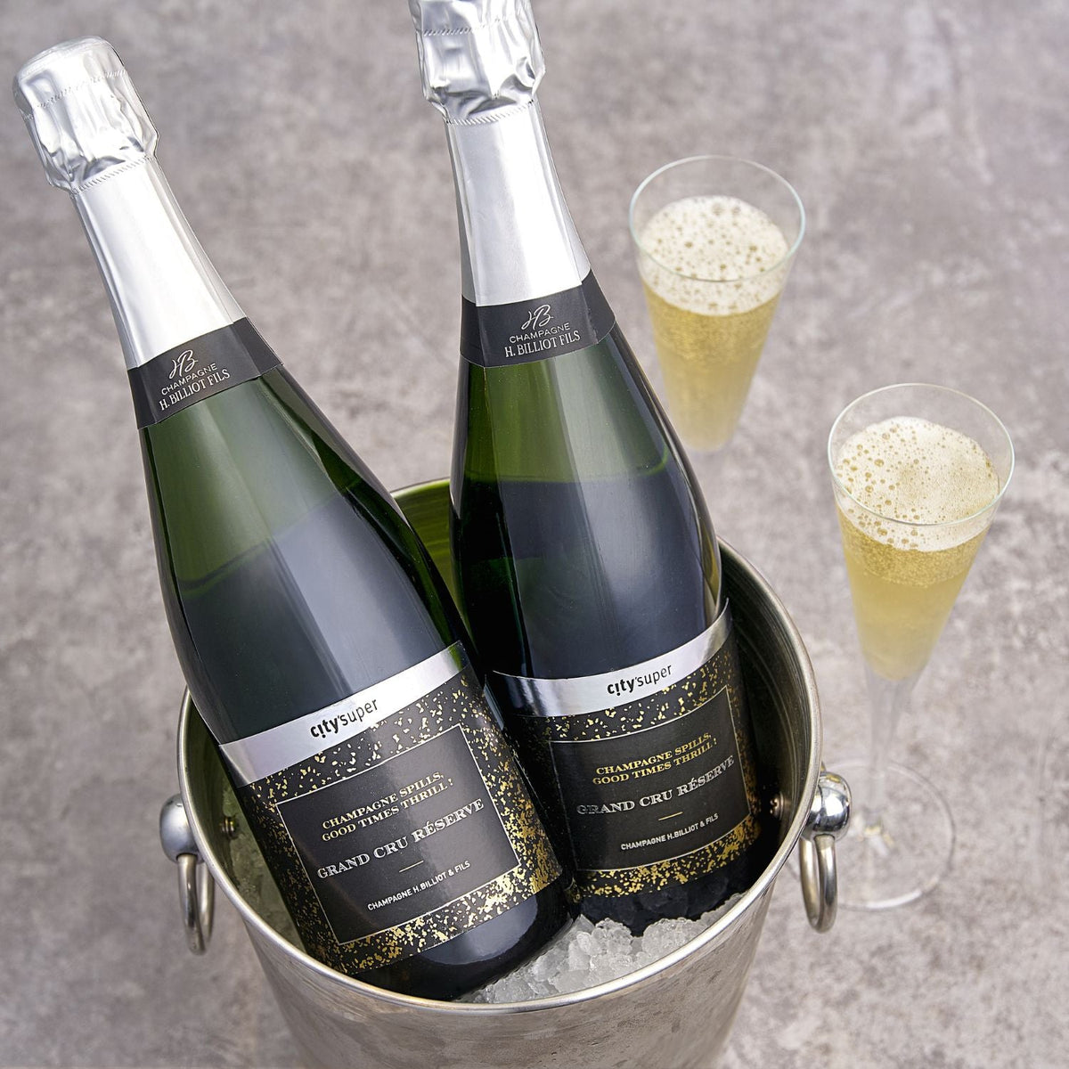 Two champagne bottles in a metal ice bucket with two filled flutes; CITYSUPER H. Billiot