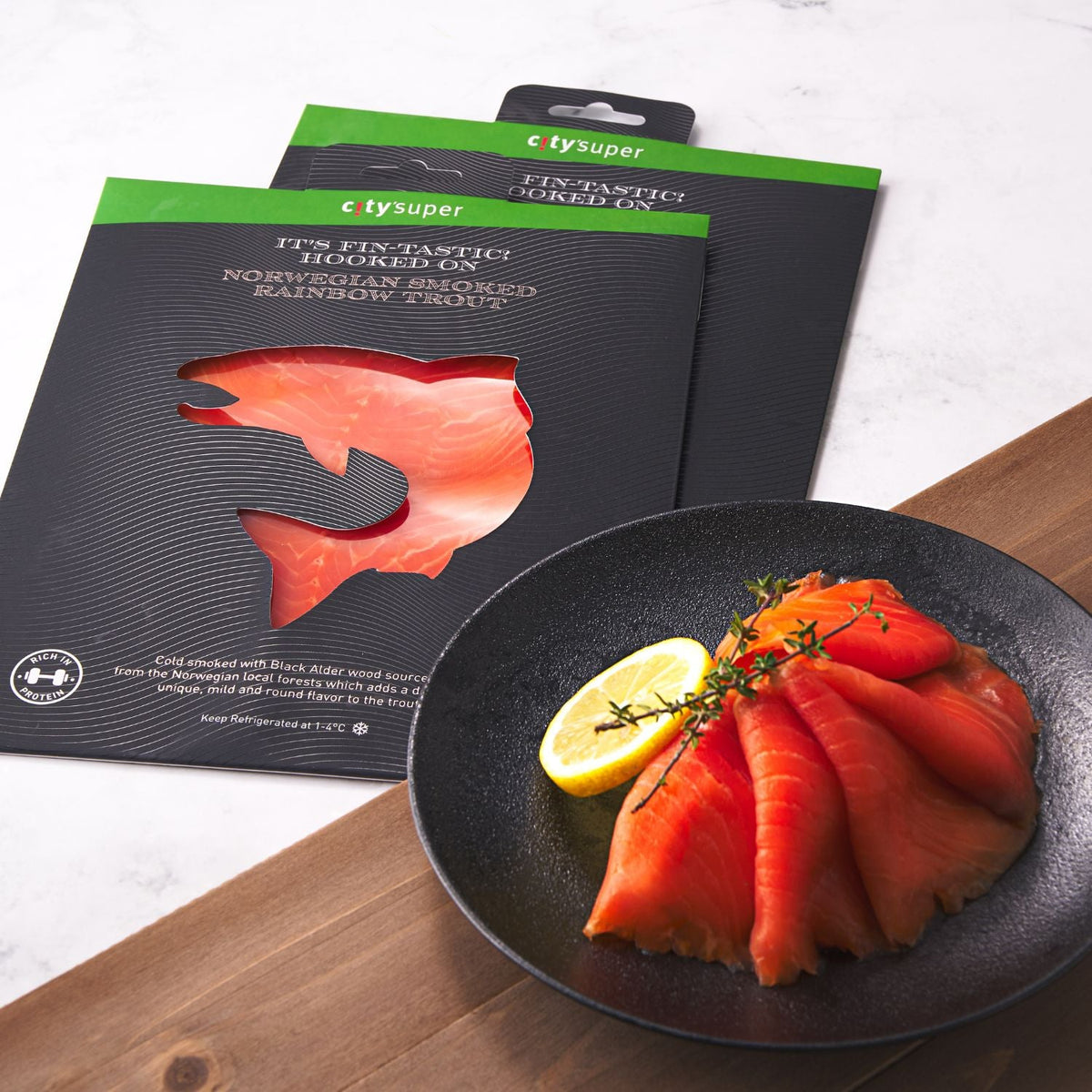 Smoked rainbow trout slices on black plate with lemon, with packaged pouch behind