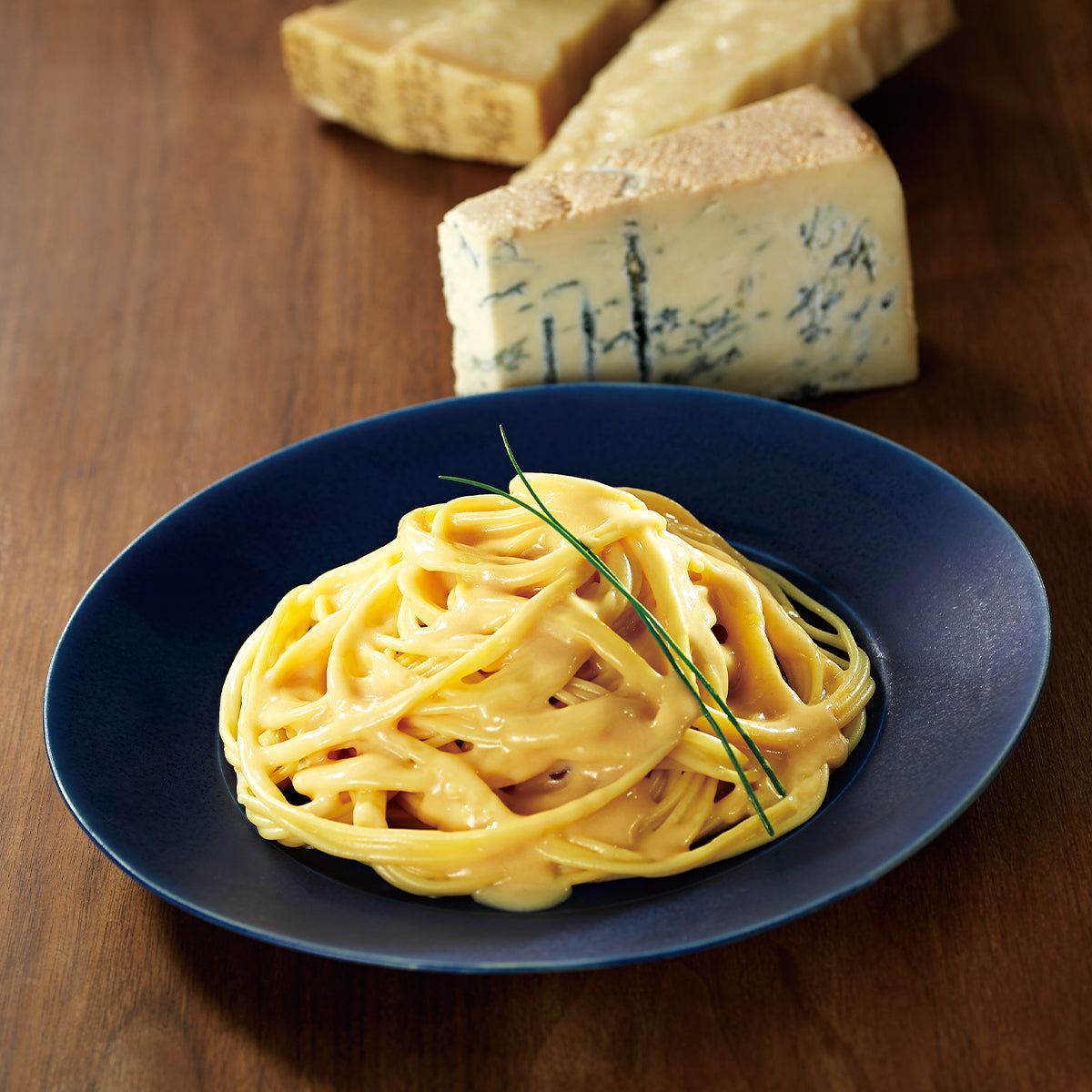 Creamy yellow quattro formaggi spaghetti in blue bowl, with cheese cubes