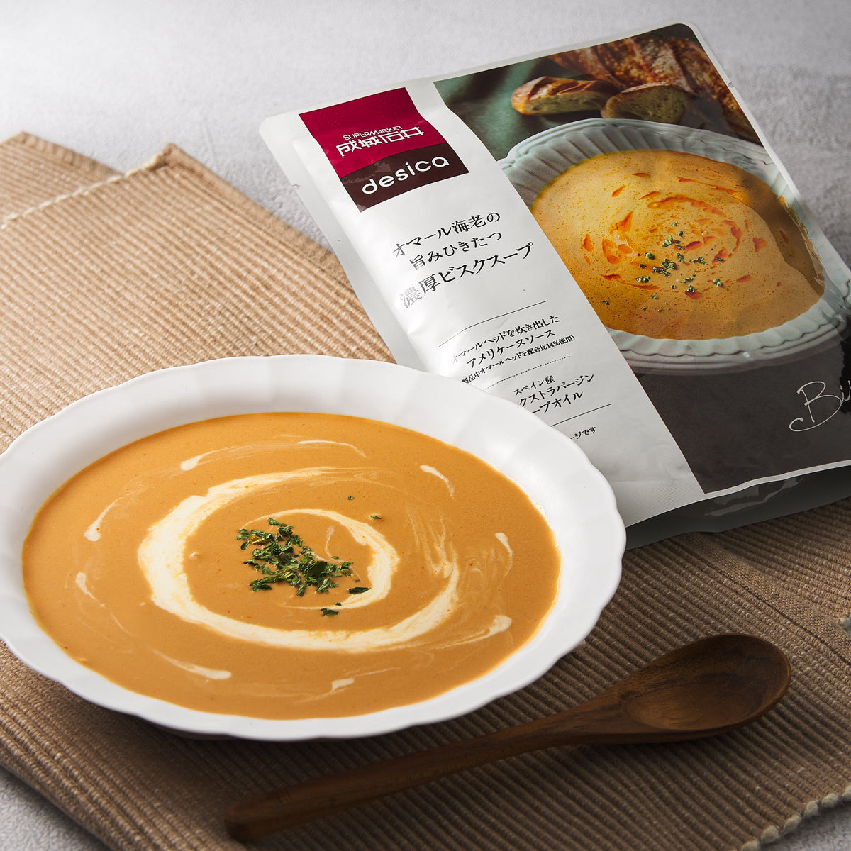 Lobster bisque soup bowl with wooden spoon beside soup pouch package
