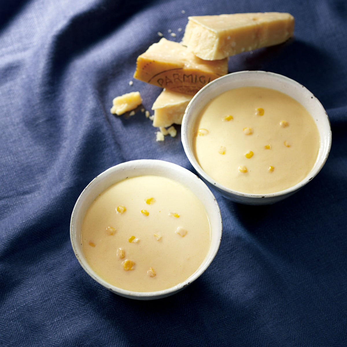Creamy corn potage soup in two bowls with parmesan cheese pieces