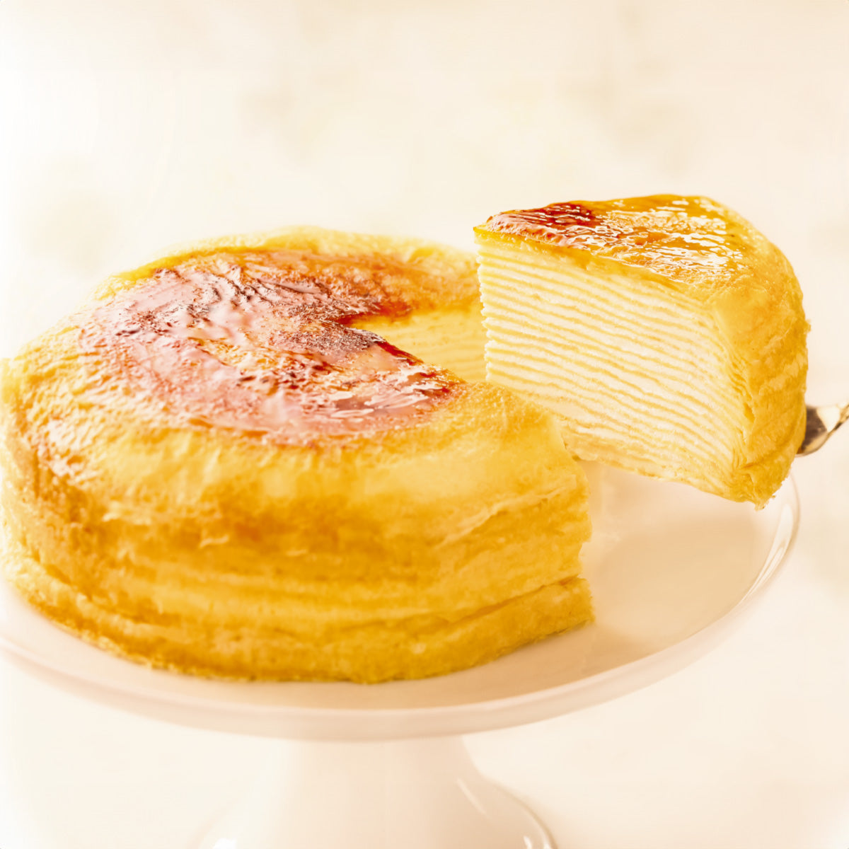 Plain mille-crepe cake with browned top, sliced and whole pieces on a plate