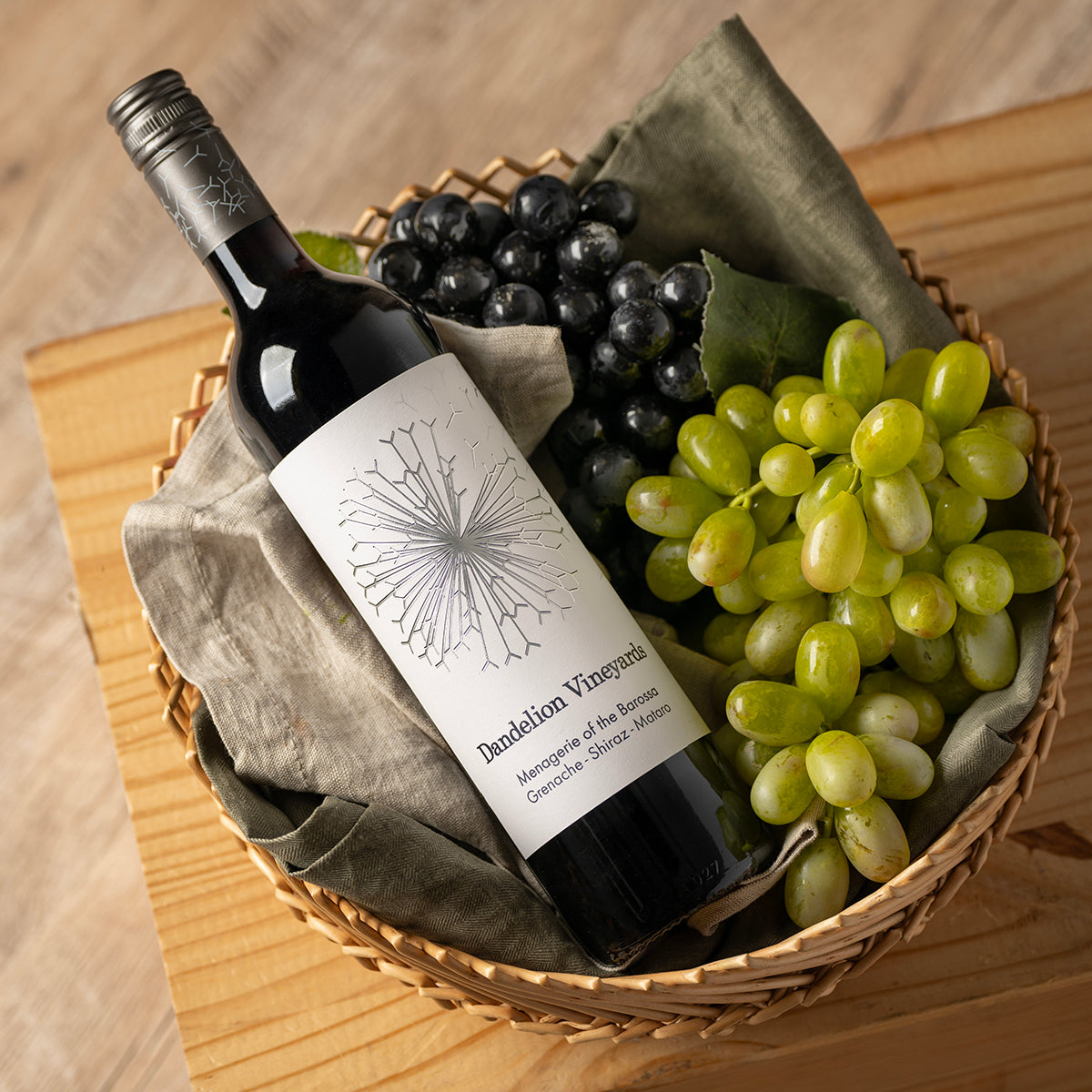 Wine bottle in wicker basket with grapes and gray cloth, Dandelion Vineyards label