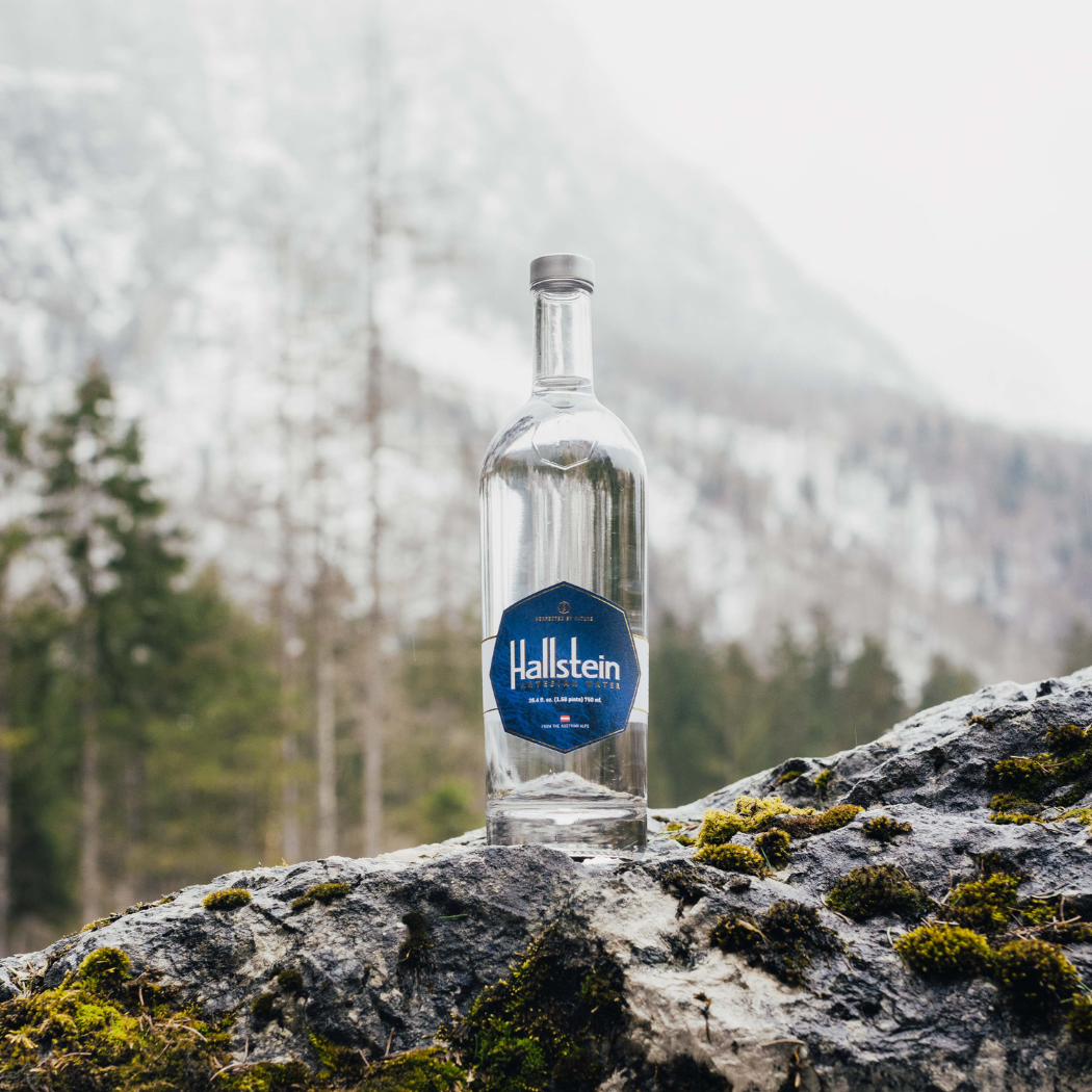 Clear artesian water bottle with blue label standing on rocks