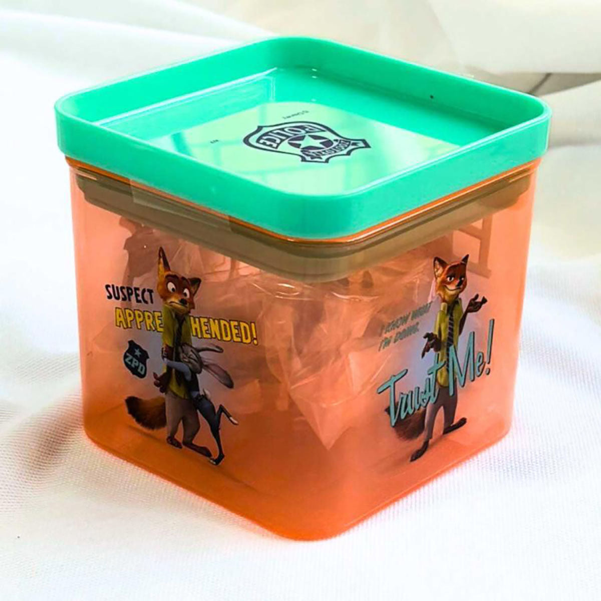 Square translucent orange confectionery container with green lid and cartoon animal graphics
