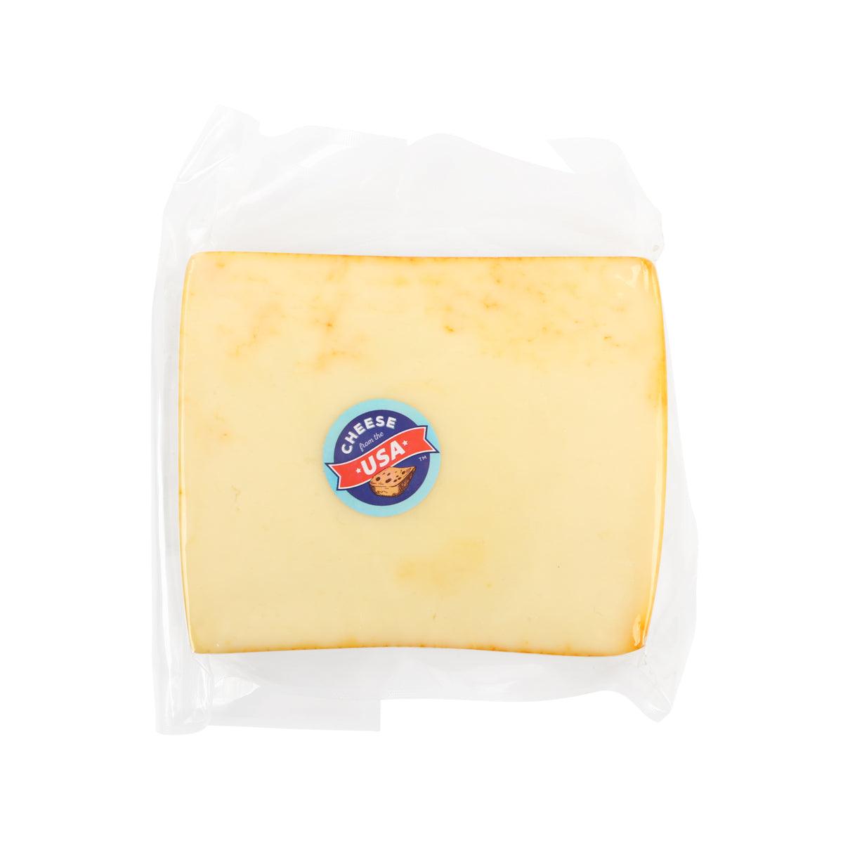 Muenster cheese wedge in clear packaging, pale yellow with brand logo sticker