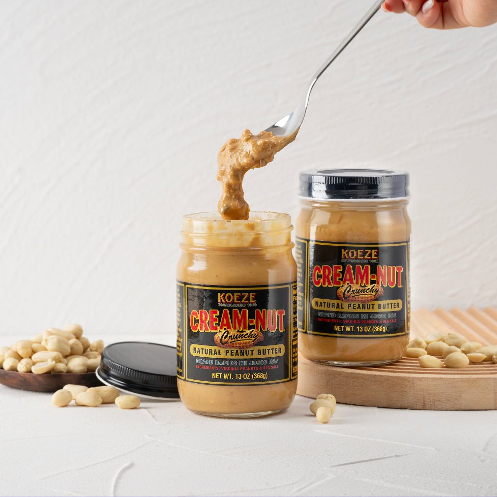 Crunchy natural peanut butter in labeled glass jar with creamy spread spoon