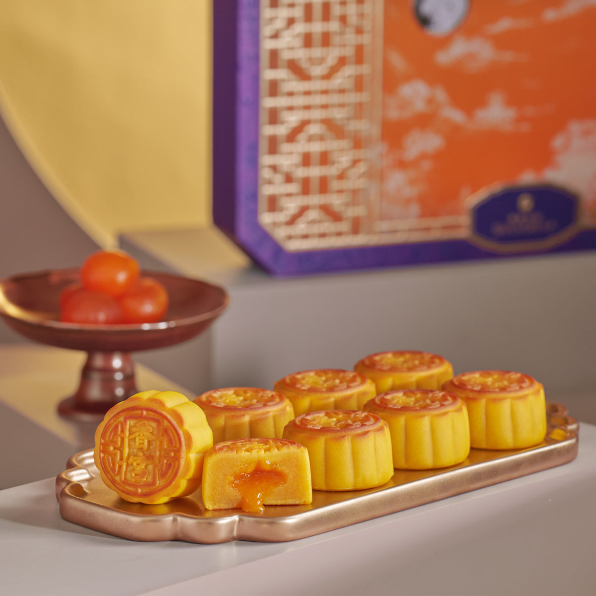 Gold mini lava egg custard mooncakes on tray, cut halves show orange filling