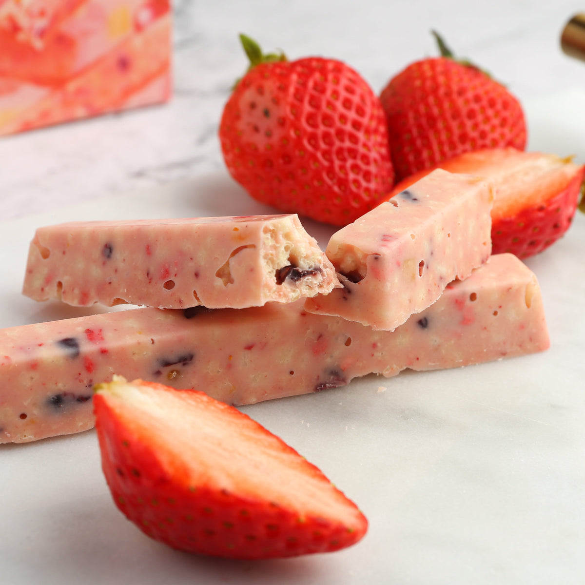 Broken strawberry fruit bar chocolate pieces with strawberries nearby.