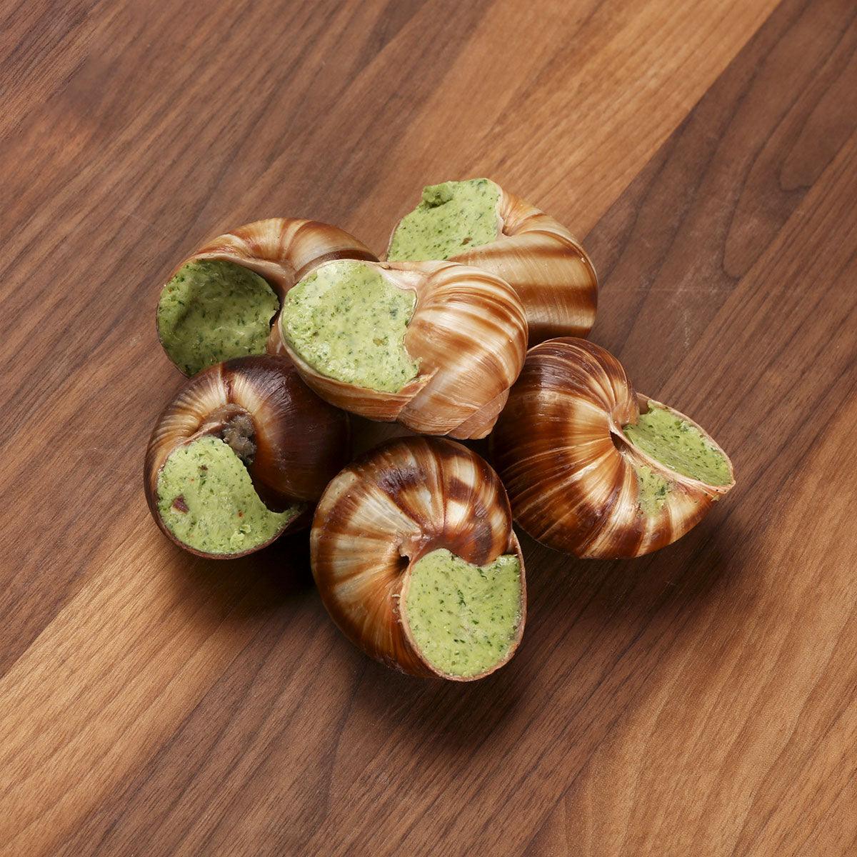 French escargot pieces cluster, brown spiral shells with green herb filling on wooden board