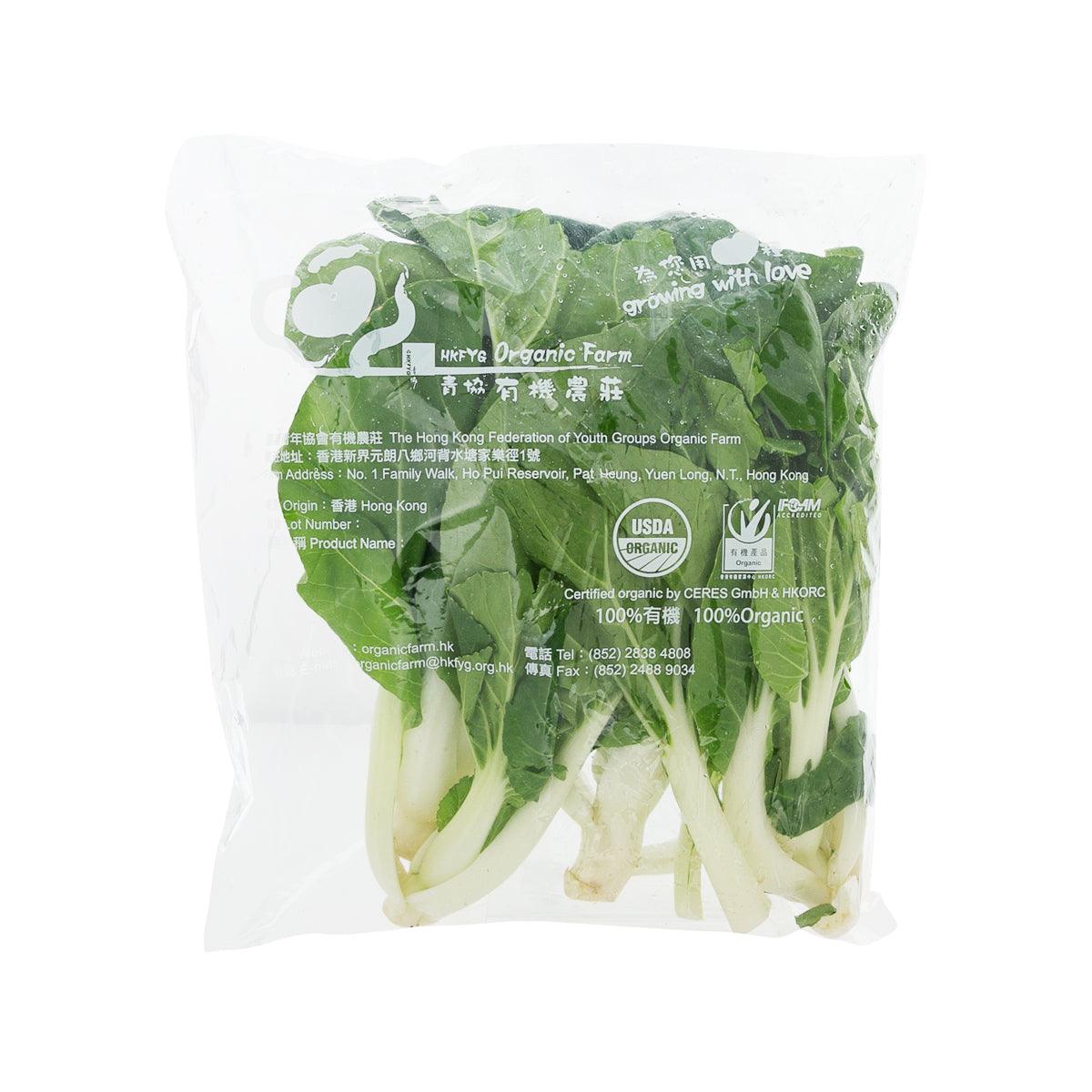 Sealed bag of green pak choi with white stems, leaf-side visible