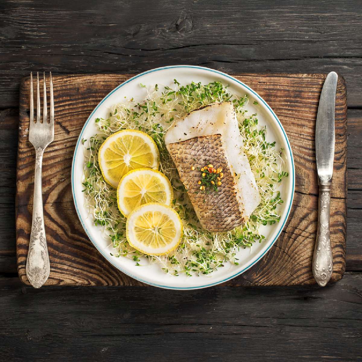 Prepared toothfish slices with scaly skin on herb greens, with lemon wedges