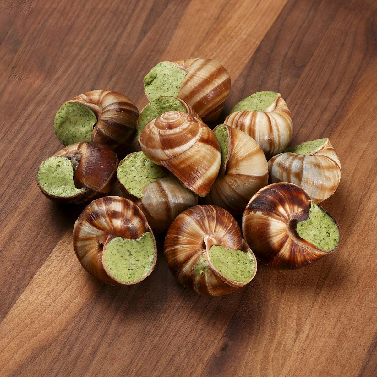French escargot pieces with green herb filling in brown spiral shells on wood surface