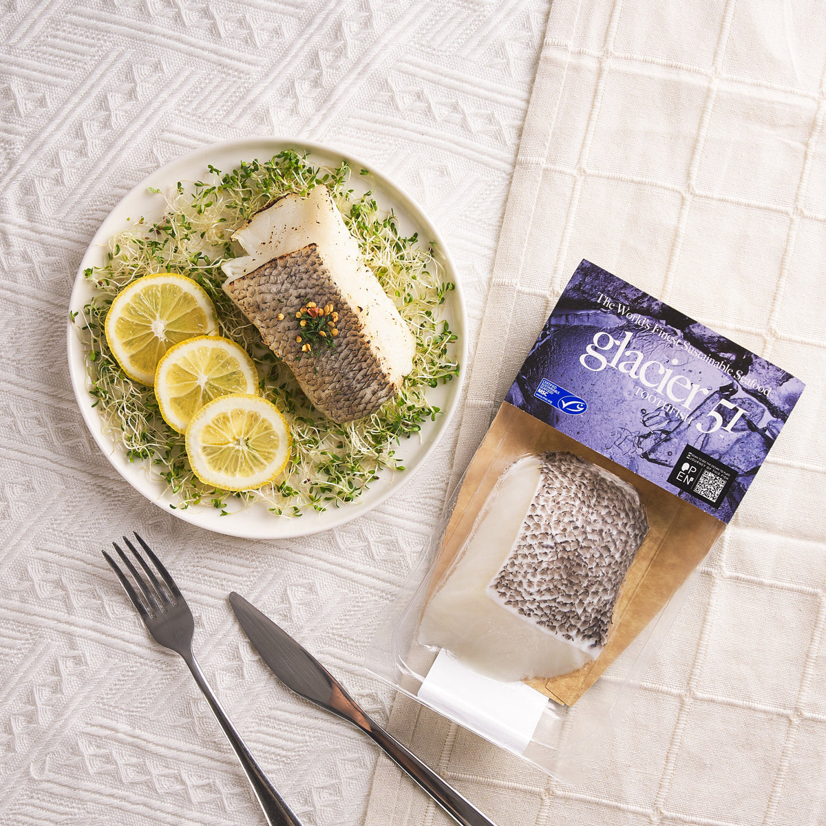 Toothfish slice in sealed pouch, with serving plate of lemon and greens