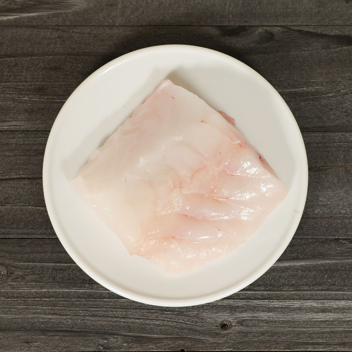 Chilled monkfish fish slice on white bowl, pale pink fillet
