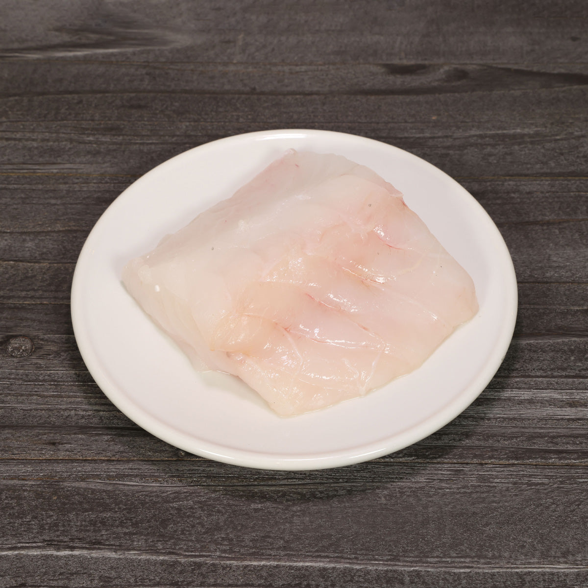 Chilled monkfish fish slice on white plate, pale pink fillet piece
