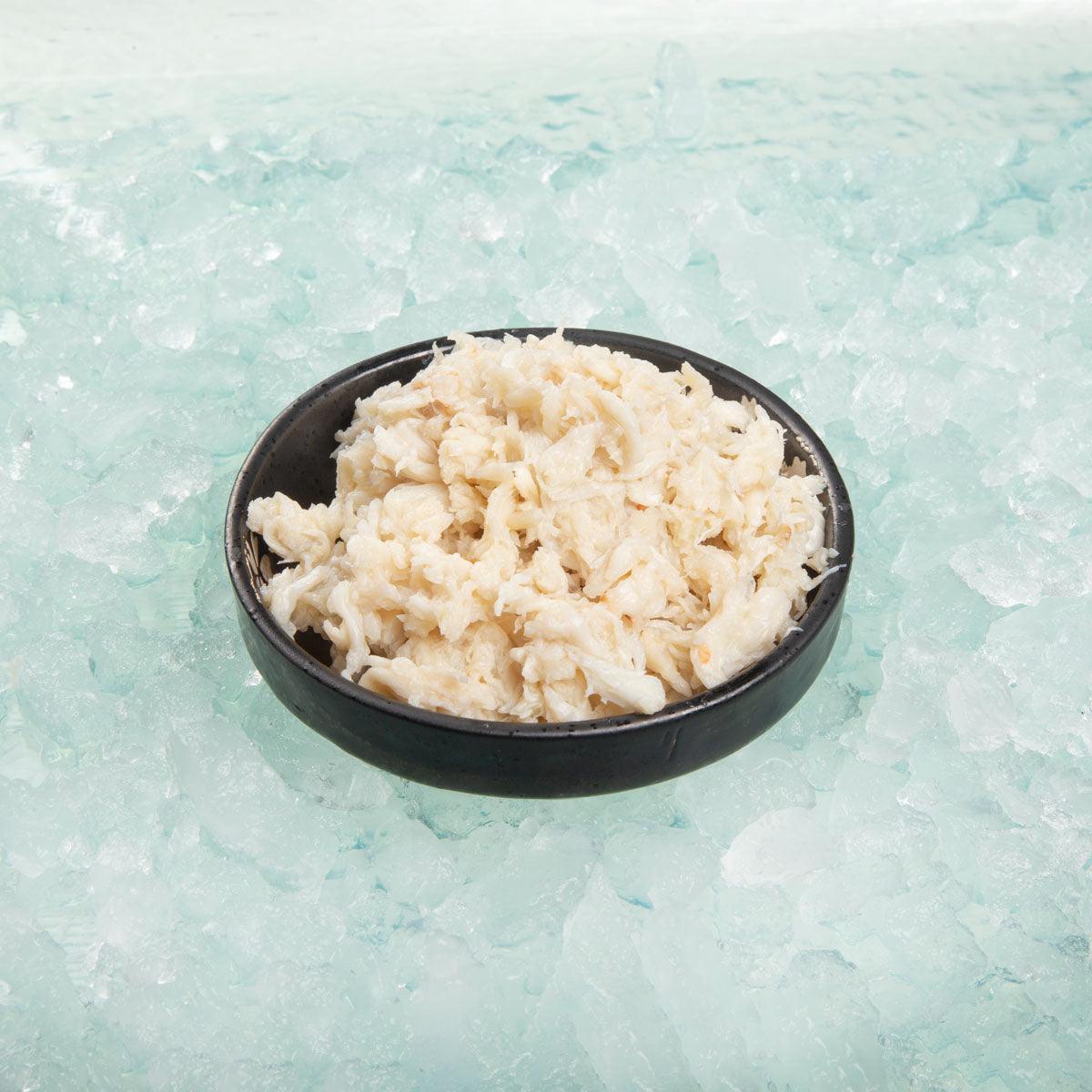 Bowl of cooked crab meat, creamy white flakes in a black serving dish.