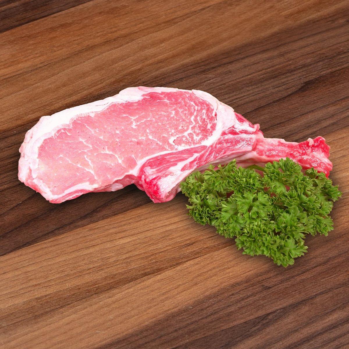 Raw pork rack chop with marbled fat, garnished with fresh parsley