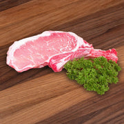 Raw pork rack chop with marbled fat, garnished with fresh parsley