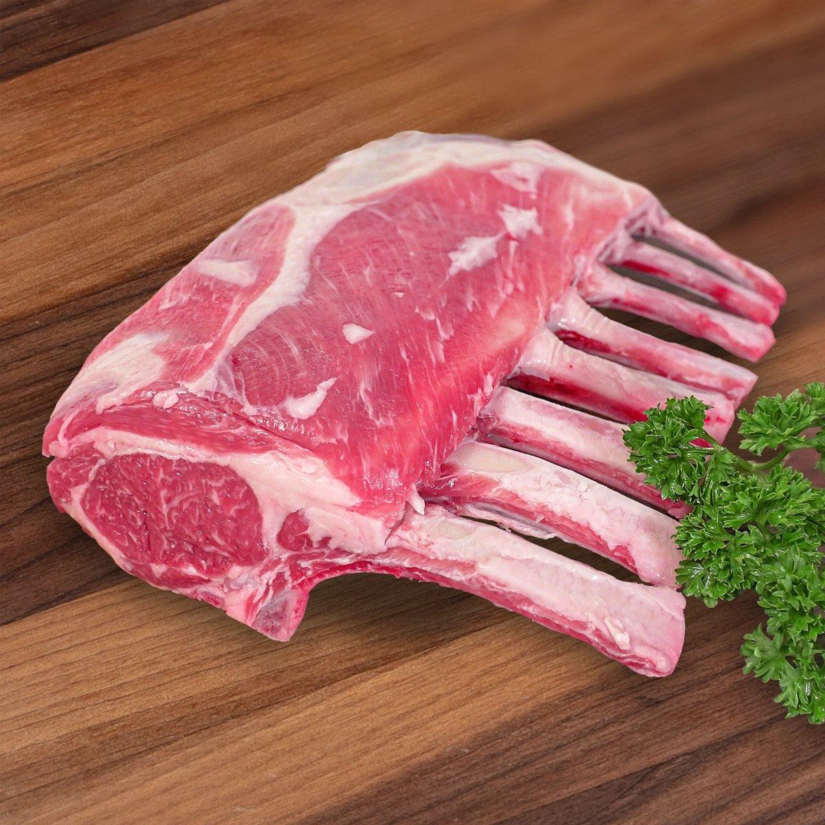Chilled raw lamb rack with exposed rib bones, pink-red meat and white fat marbling