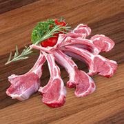 Raw organic lamb rack chops with rib bones and fresh herbs on wooden board