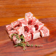 Cubed organic beef for stewing, visible marbling with small herb sprigs
